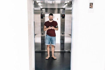Man in summer clothes using a mobile phone inside an elevator