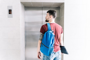 Man with a laptop in his hand and a blue bag in front of an elevator