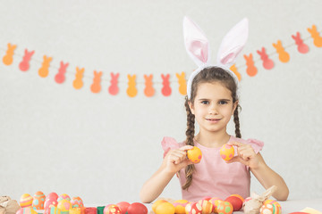 Cute little girl holding colorful easter eggs with bunny ears on her head on a white background. The kid smiles and prepares for the holiday of colorful happy Easter