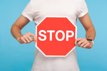Closeup of man in white t-shirt holding Stop symbol in hands, warning with red traffic sign,...