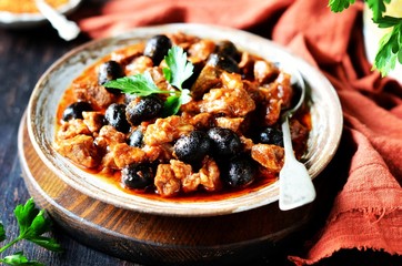 Beef stew with olives and tomatoes on a dark background, rustic