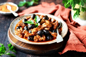 Beef stew with olives and tomatoes on a dark background, rustic