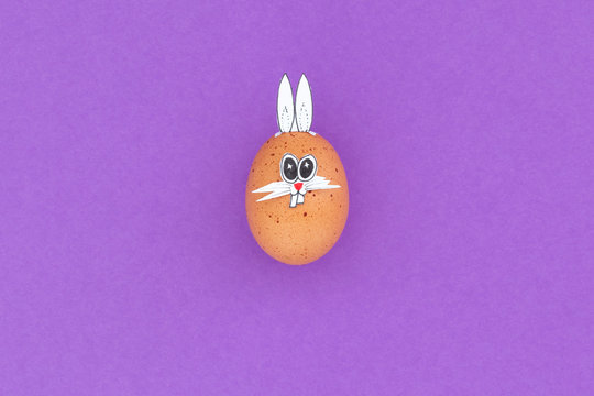 Brown easter egg with funny bunny ears and cartoon face on purple background