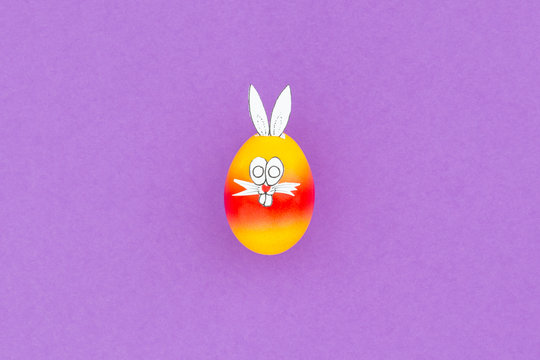 Colorful painted easter egg with funny bunny ears and cartoon face on purple background
