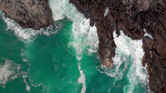   Aerial view of the coast of the Atlantic Ocean in a cinematic shot where the drone is moving forward in a zenith shot from the turquoise water towards the cliff rocks