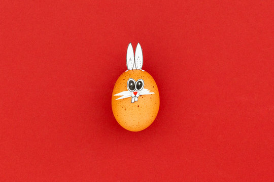Brown easter egg with funny bunny ears and cartoon face on red background