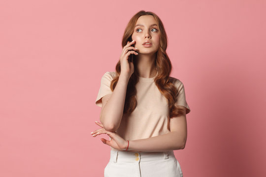 young attractive female talking with cell phont looking left over pink background