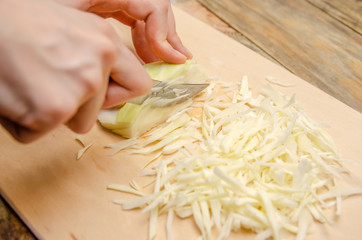 Women's hands were chopping cabbage on a wooden plank. Chop fresh cabbage