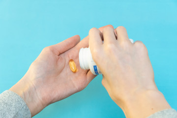 One hand pours yellow vitamin capsules into the other hand on a blue background
