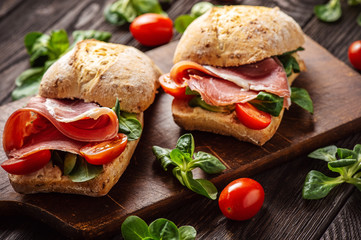 Jamon sandwiches with tomatoes, on wooden board.