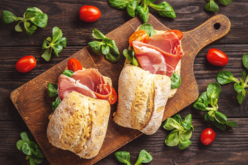 Jamon sandwiches with tomatoes, on wooden board.