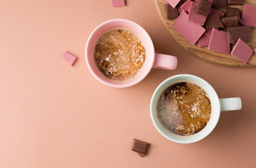 two cups of coffee with milk on a brown background next to chocolate. copy space