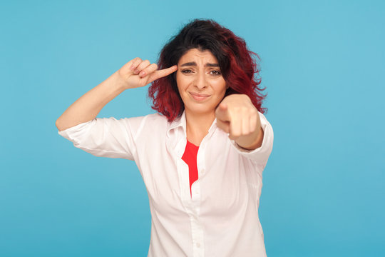 Your stupid idea. Portrait of hipster woman with fancy red hair showing dumb cuckoo gesture and pointing to camera, dissatisfied with senseless talk. indoor studio shot isolated on blue background