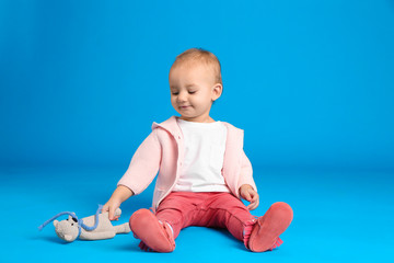 Cute little child playing with knitted toy on light blue background