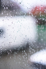 Window overlooking a rainy street. Gloomy evening weather with a view of the road. Drops on glass and bokeh from cars. Stock background for design