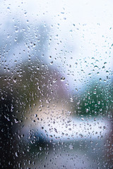 Window overlooking a rainy street. Gloomy evening weather with a view of the road. Drops on glass and bokeh from cars. Stock background for design