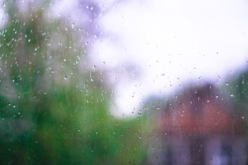 Window overlooking a rainy street. Gloomy evening weather with a view of the road. Drops on glass and bokeh from cars. Stock background for design