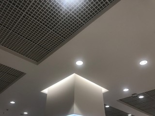  Suspended Grid false ceiling with gypsum bulkhead design and column coves with indirect lighting for a lucrative design view for a shopping mall and emulsion painted ceiling which has down lights