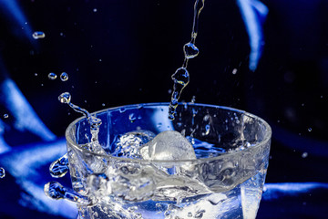 Water splash in glass with ice. Blue silk background