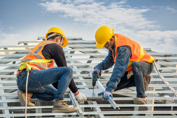 Construction worker wearing safety harness belt during working installing concrete roof tile on top...