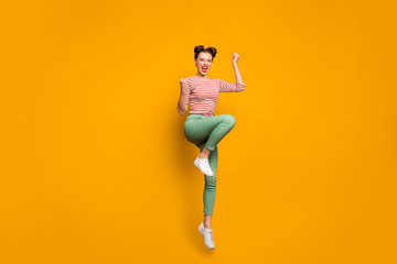 Fototapeta na wymiar Full length photo of pretty attractive lady traveler jumping high up raise fists scream astonished wear striped red white shirt green trousers sneakers isolated yellow color background