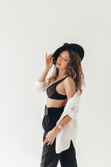 The concept of a trendy modern fashion trend shooting in a photo Studio , a beautiful sexy attractive gentle daring girl in a black hat, in black underwear, in a large shirt posing on a white backgrou