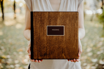 book for photos with the inscription wedding in a wooden cover in the hands of a girl on a blurred background