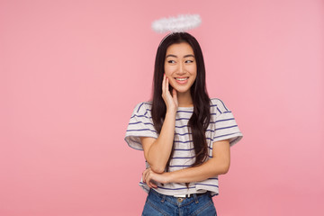 Portrait of lovely angelic asian girl with long brunette hair and halo over head timidly touching face and smiling, dreaming with shy modest expression. indoor studio shot isolated on pink background