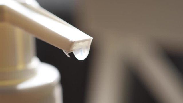 The tip of an antiseptic agent comes into focus with a droplet at the top of a spray nozzle