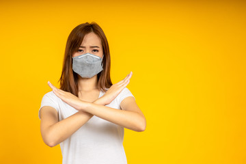 Asian woman made a cross and wearing hygienic mask to protect virus, COVID 19 or Colona Virus infection and dust PM 2.5 pollution isolate on yellow background