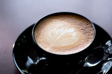 Coffee latte art in ceramic black cup on the wooden table background, increase energy for today.