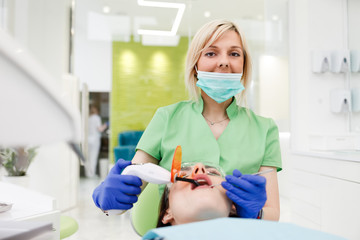 Portrait of female dentist doctor who puts a dental filling to a patient using uv lamp. Dental treatment process