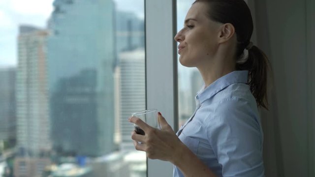 Young happy businesswoman drinking whiskey and admire view from window