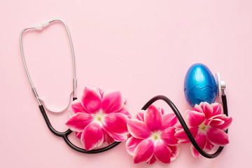 Stethoscope, spring flowers and blue easter egg on pink background with a copy space