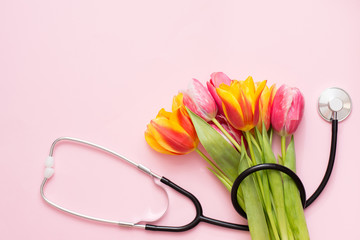 Stethoscope and colorful tulips on a pink background with a copy space