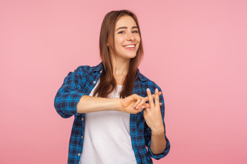 Internet trends. Portrait of charming happy girl in checkered shirt crossing fingers to make hashtag sign and looking at camera with toothy smile. indoor studio shot isolated on pink background