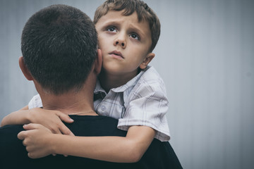 Portrait of young sad little boy and father standing outdoors at the day time.