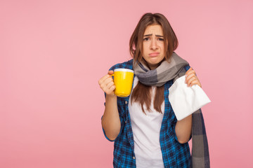 Treatment of seasonal influenza. Portrait of sick girl wrapped in scarf looking with funny displeased grimace, holding tea cup treating flu, cough and fever. studio shot isolated on pink background