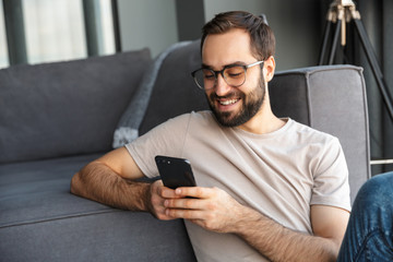 Attractive smart young man sitting on a floor in the living room