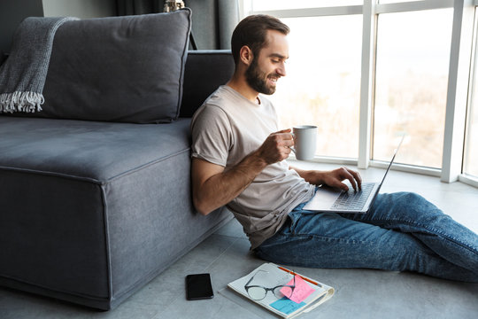 Attractive smart young man sitting on a floor in the living room - Powered by Adobe