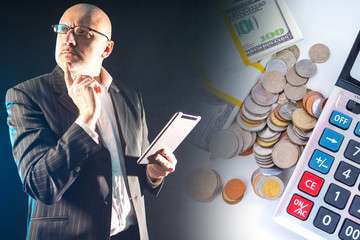 A man with glasses is holding a tablet against the background of money and a calculator. Financial...