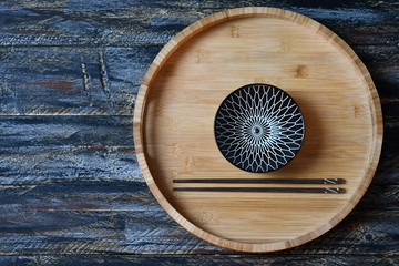 A bowl & brown chopsticks on a tea tray on a multi-colored surface