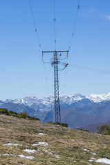 High voltage power line tower, with electrical bypass in the middle of the mountains, with snow in the background.