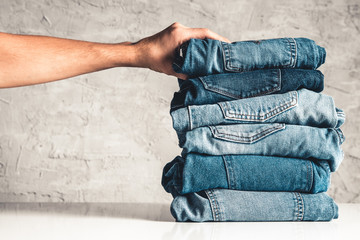 Hands, put the stack of blue jeans on gray background.