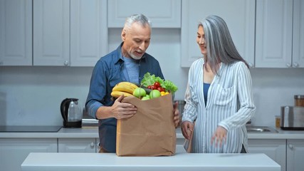 senior and interracial couple putting fruits and vegetables on table - Powered by Adobe