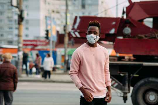 A young African man stands with a medical protective mask on his face at city street.