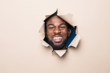 Handsome young african man with head through beige paper hole