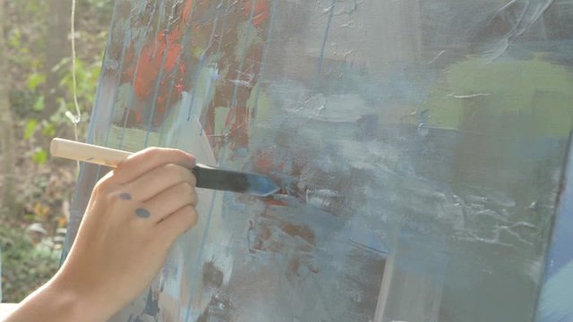Young female professional artists dabs brush on abstract multicolored painting during the day at sunset, slow motion