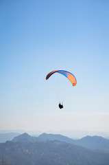 Fototapeta na wymiar Paracaídas azul y naranja con paracaidista en el cielo deporte extremo