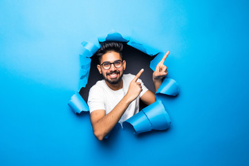 Young handsome indian bearded man pointed side look from blue paper hole